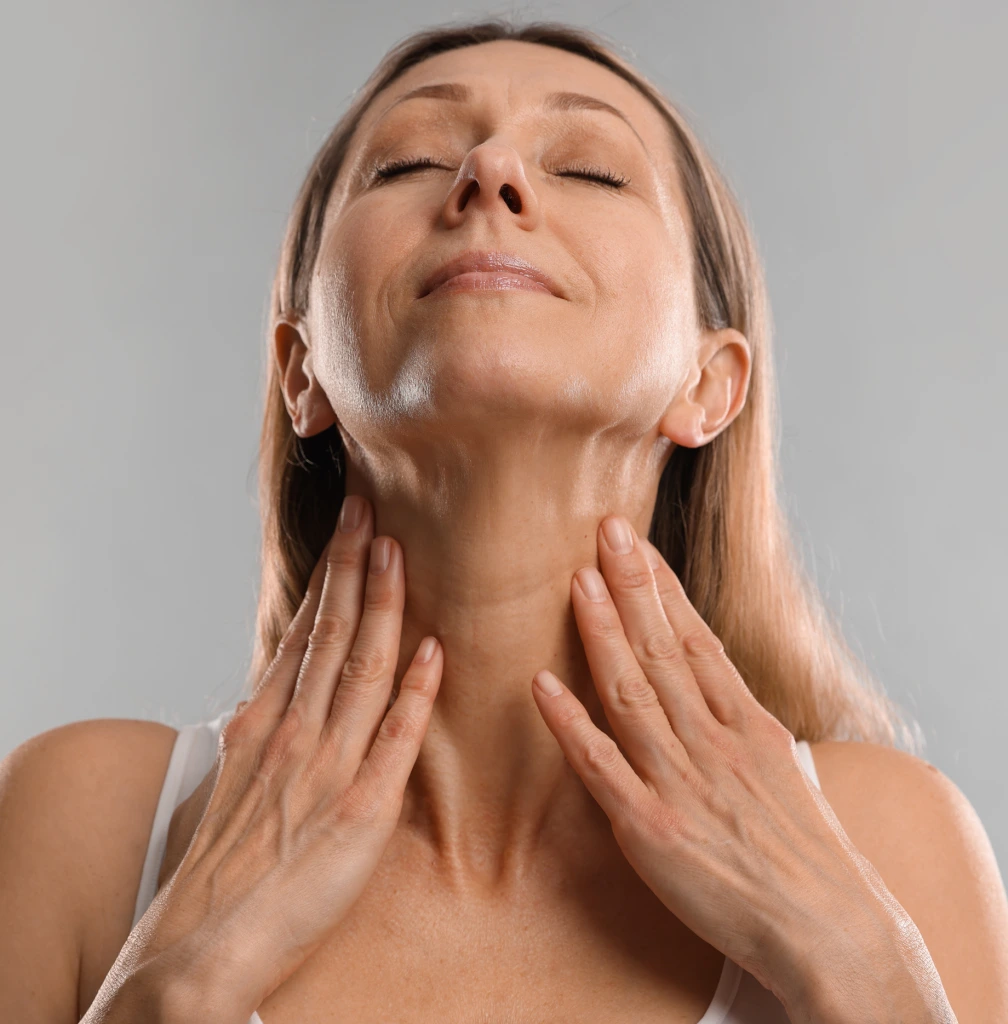 Woman touching her neck and jawline with both hands, demonstrating neck lift treatment area
