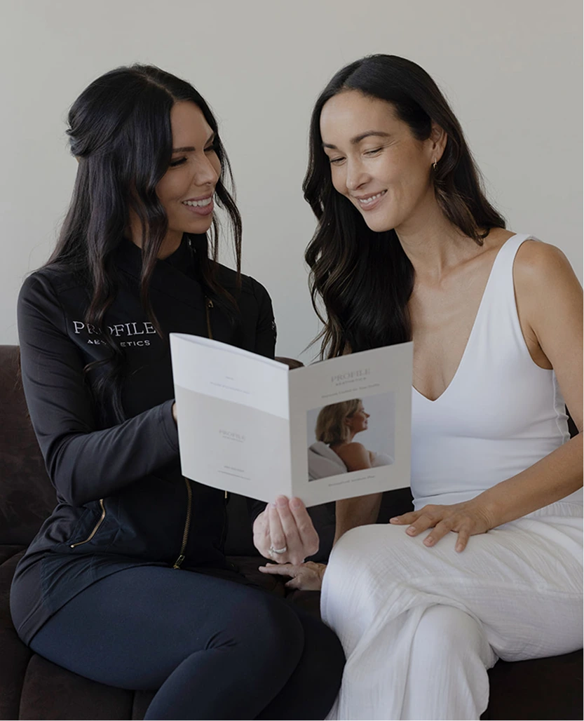 Profile Aesthetics provider in black jacket reviewing RF microneedling treatment brochure with smiling patient in white top