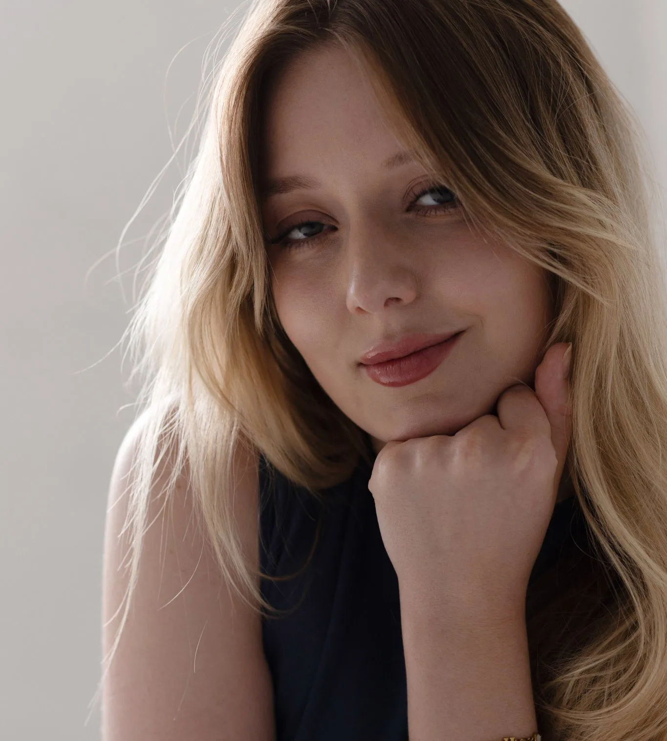Woman with smooth, glowing skin and long blonde hair touching her face against neutral background