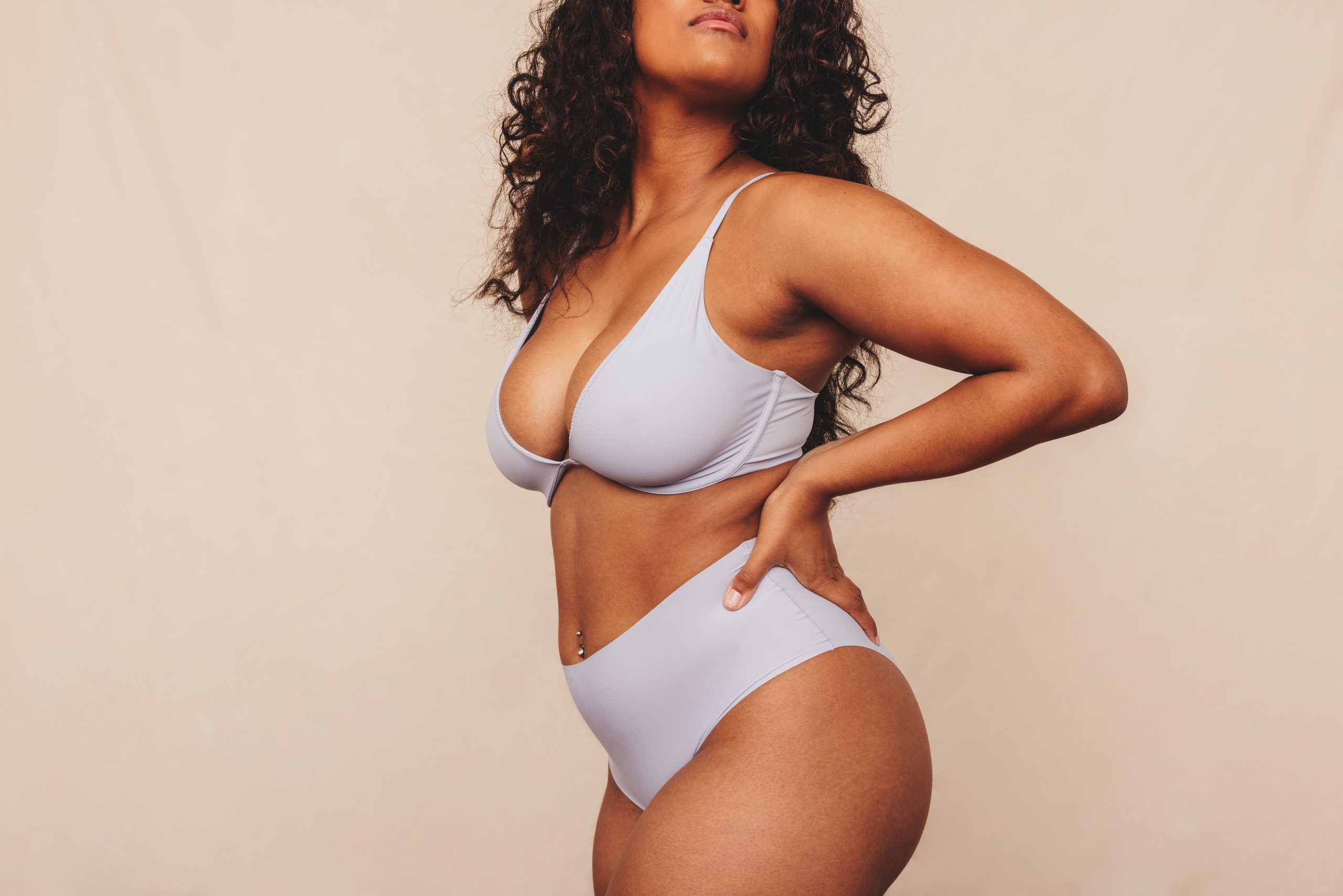 Woman in white bikini posing with hand on lower back against neutral background