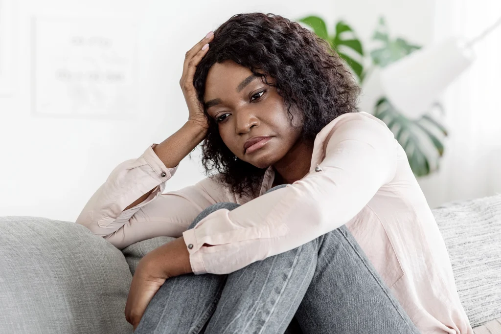 African American woman sitting on a sofa, looking distressed with her head in her hand