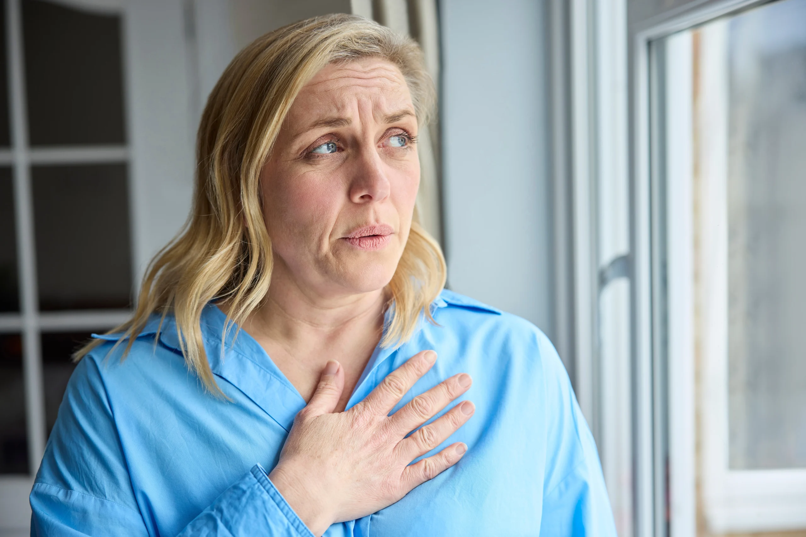 Woman holding her hand to her chest while looking out a window
