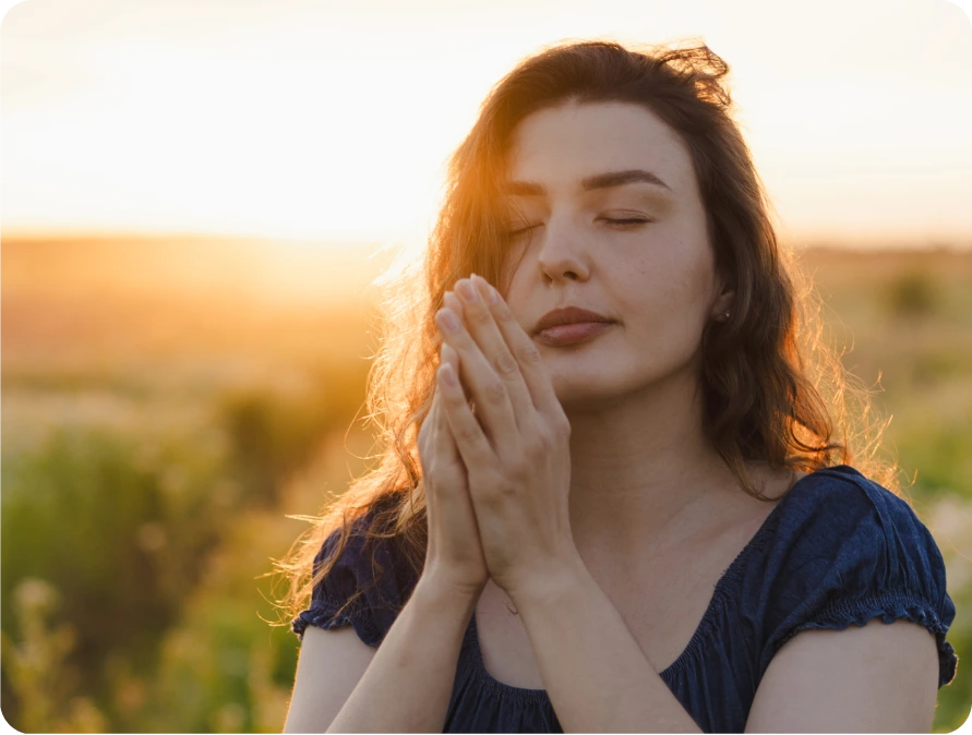 Woman with hands pressed together at sunset