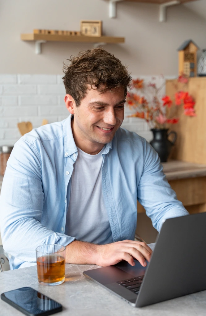 Man smiling while using a laptop at a kitchen table