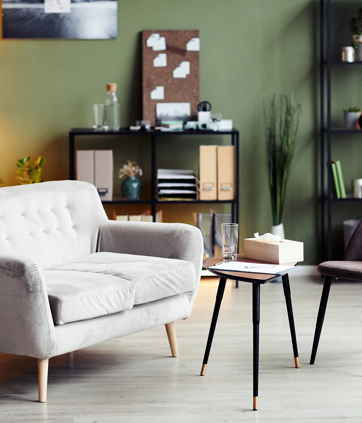 Calming therapy room with cream armchair, small side table, storage shelving, and green accent walls at the practice's Main Office