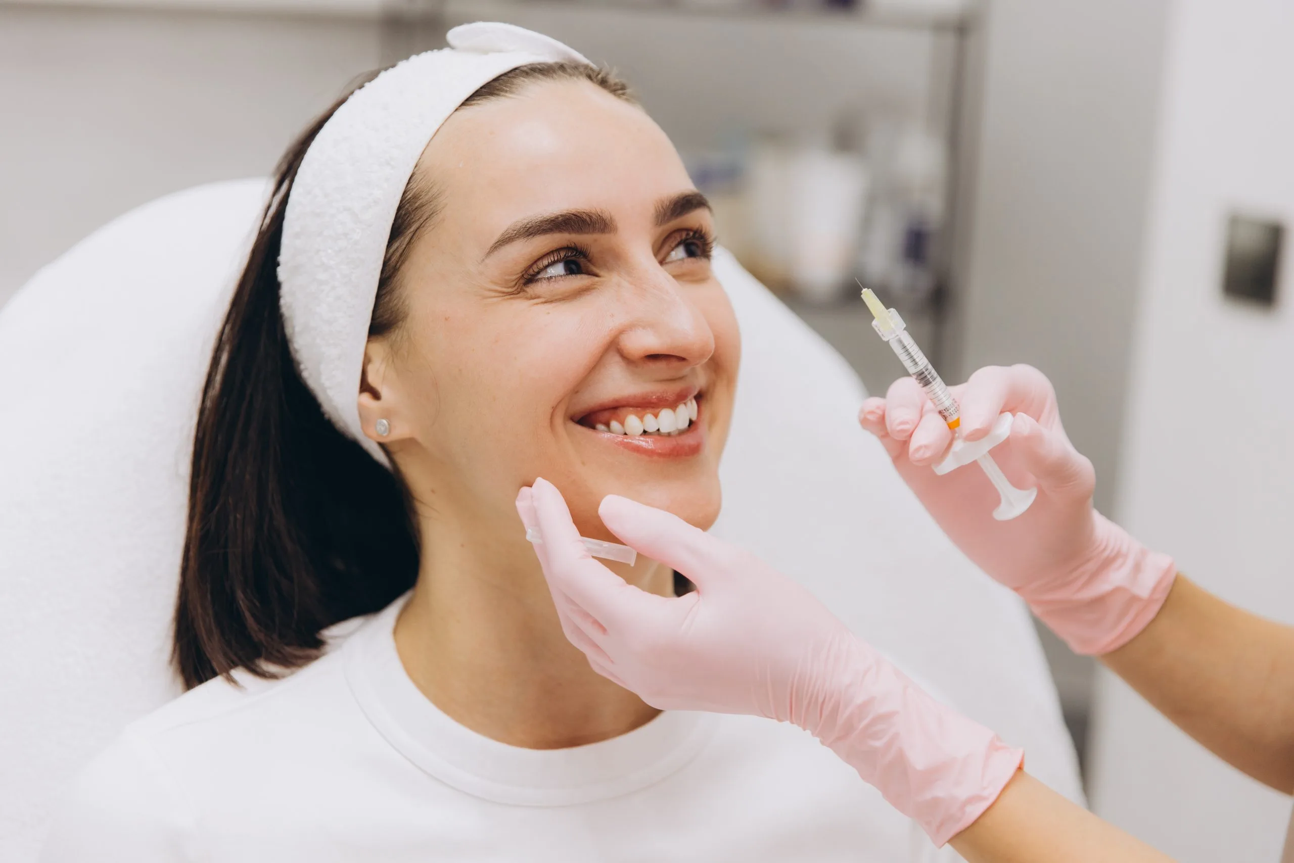 Healthcare provider in pink gloves holding syringe near patient's face during injection treatment