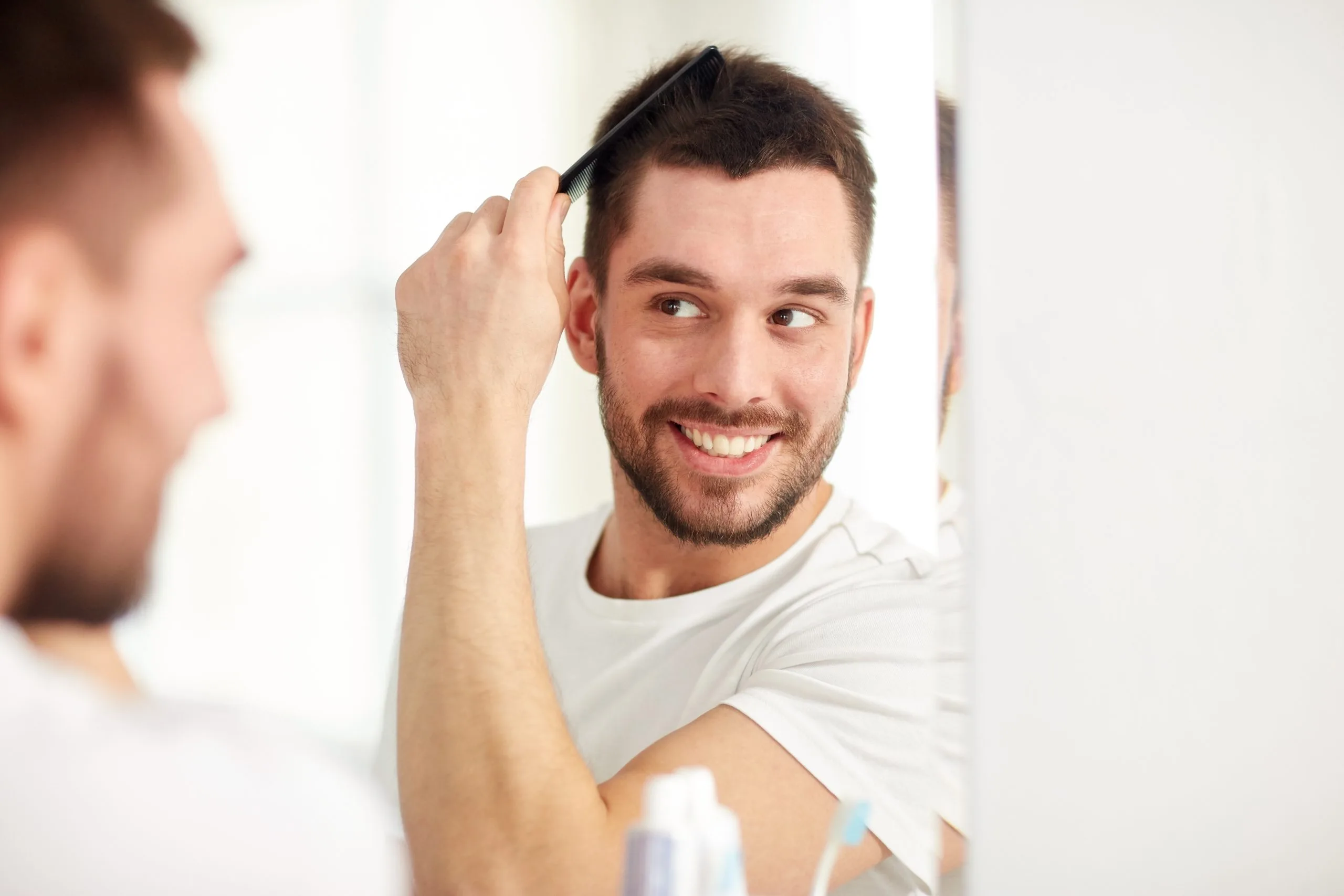 Man examining his hair in mirror while smiling