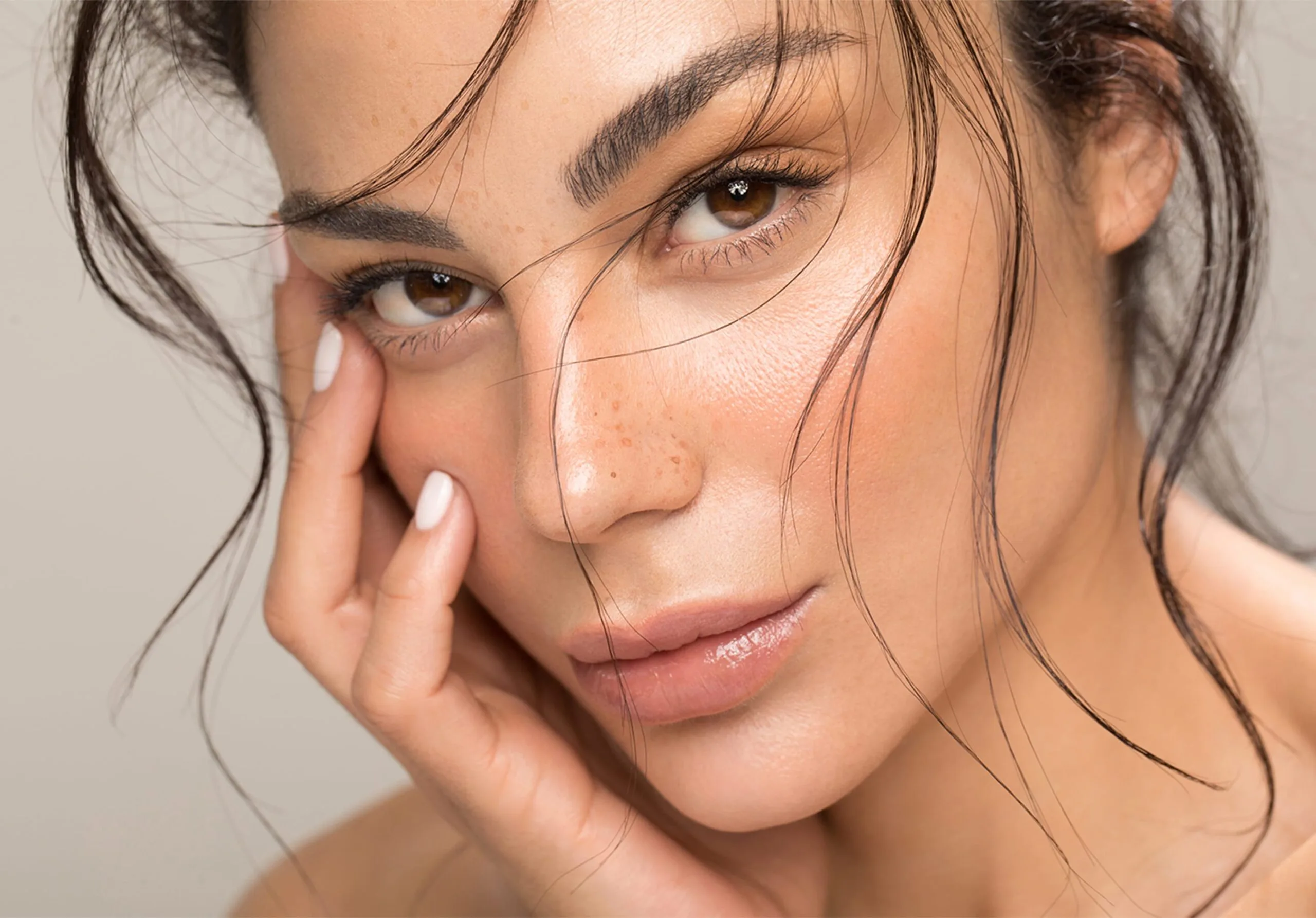 Woman with smooth, glowing skin touching her face against a neutral background