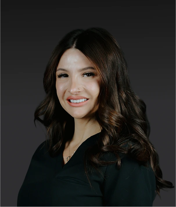 Woman with long dark wavy hair smiling at camera against gray background