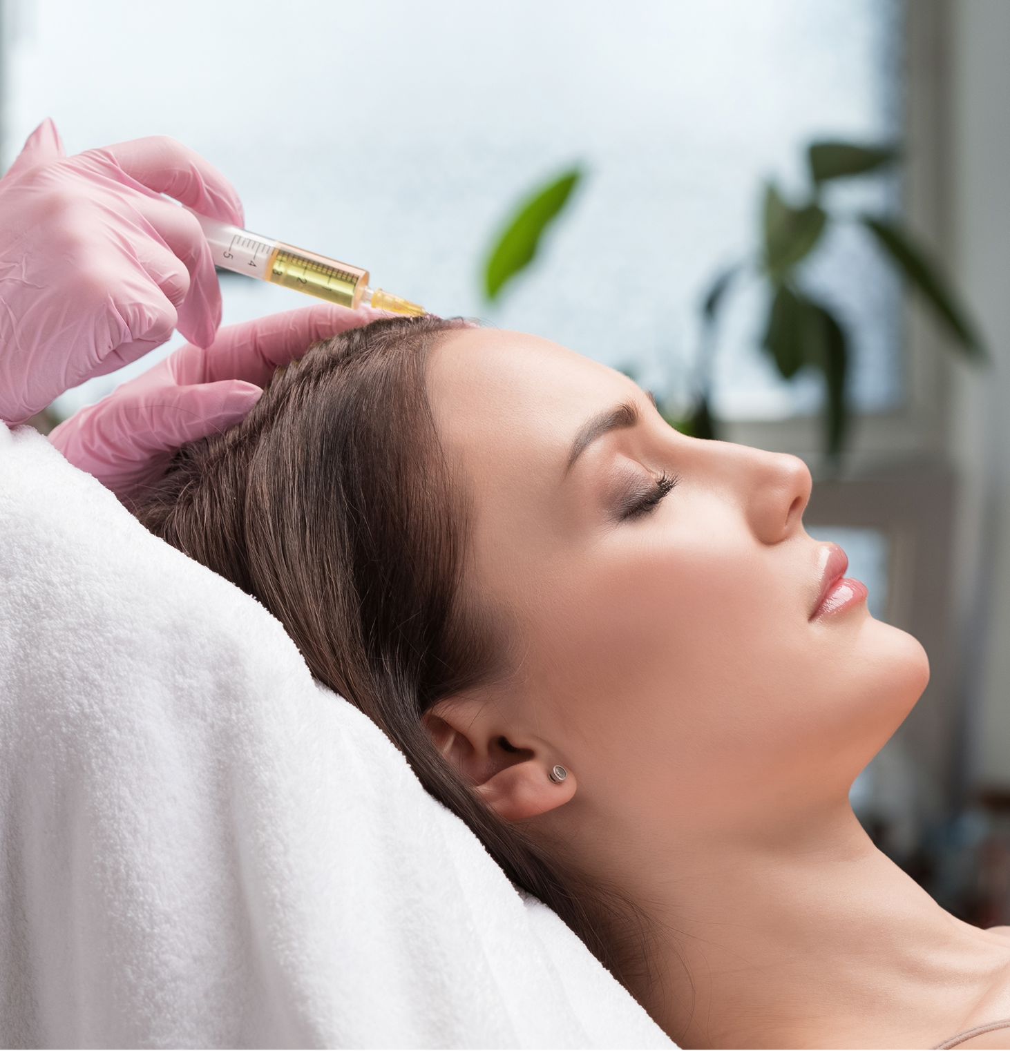 Clinician in pink gloves injecting PRP solution into patient's temple during facial rejuvenation treatment