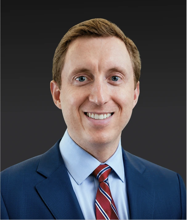 Professional headshot of a man in a dark blue blazer and red striped tie smiling at the camera