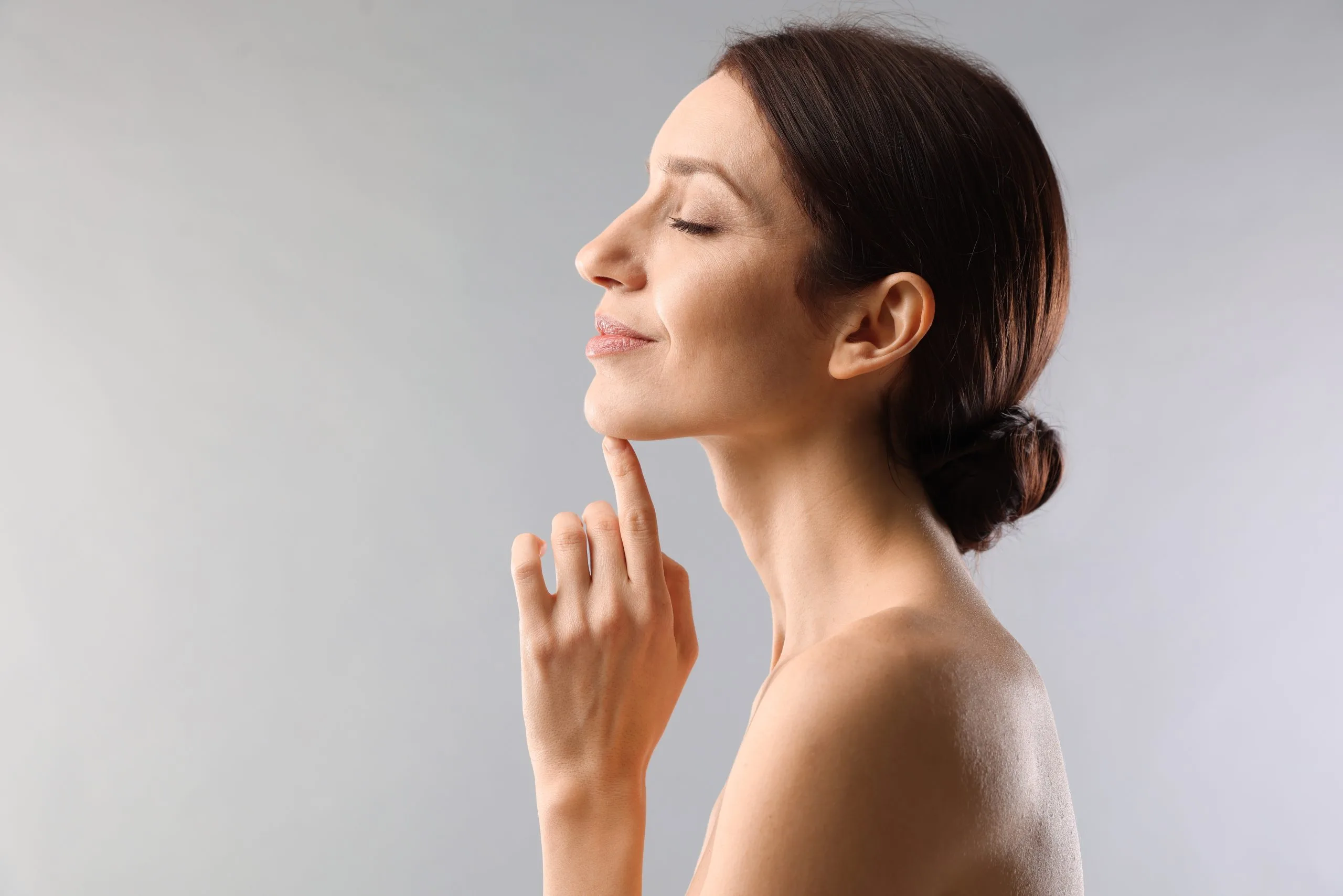 Woman touching her face in profile against a neutral background