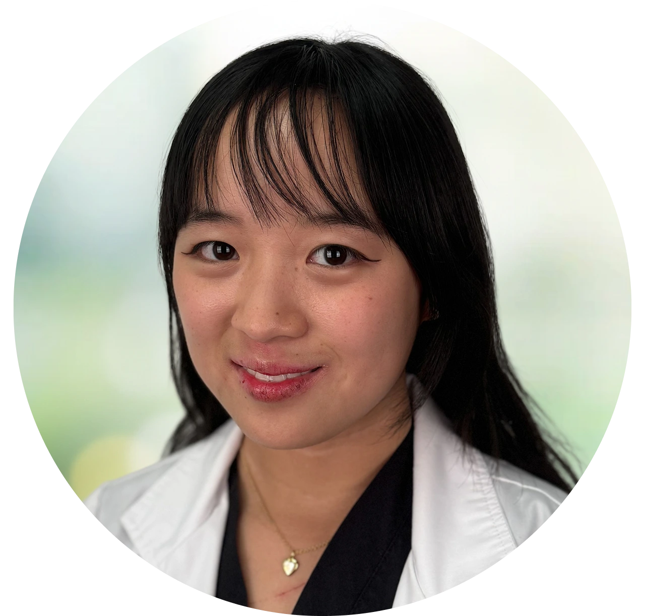 Professional headshot of woman with black hair and white coat against blurred green background