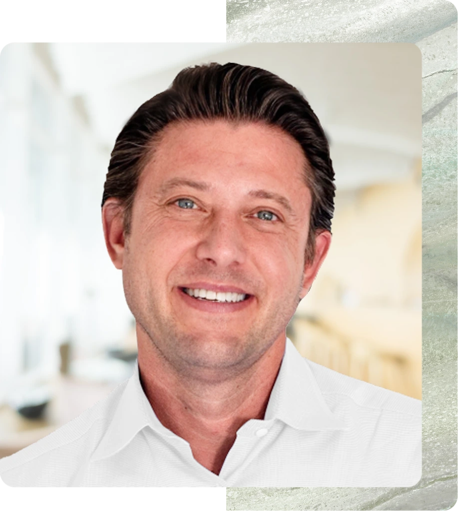 Man with dark hair and blue eyes wearing white button-up shirt in medical office setting