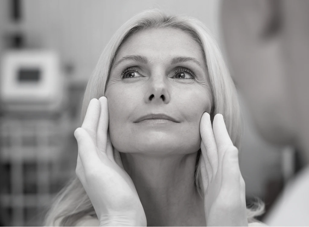 Woman touching her face with both hands, looking upward in a clinical setting