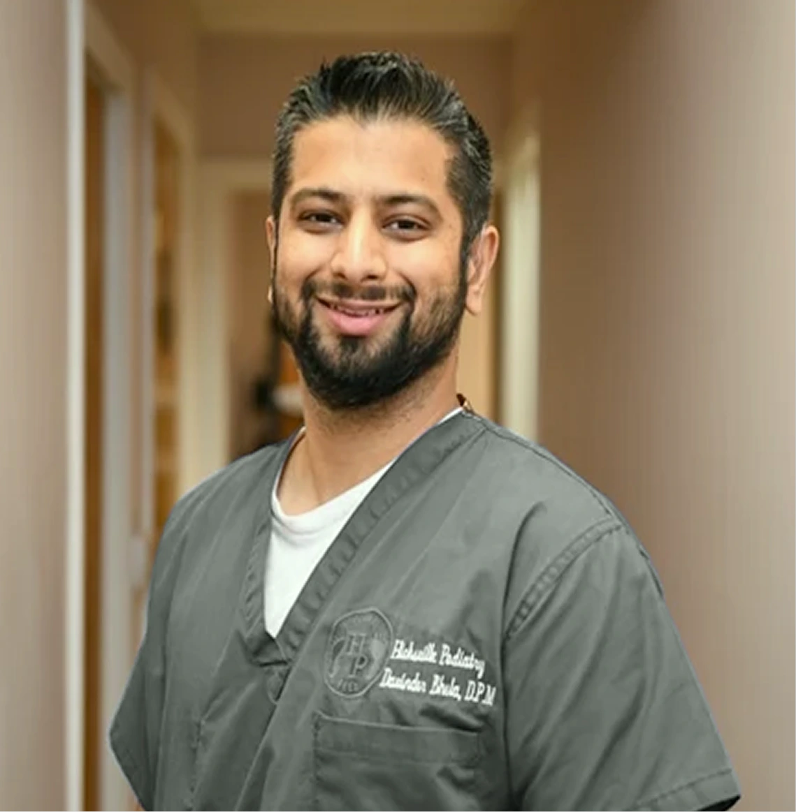 Dr. Davinder Bhela, founder of Restore Podiatry & Laser Center, smiling in clinical scrubs at the Hicksville office