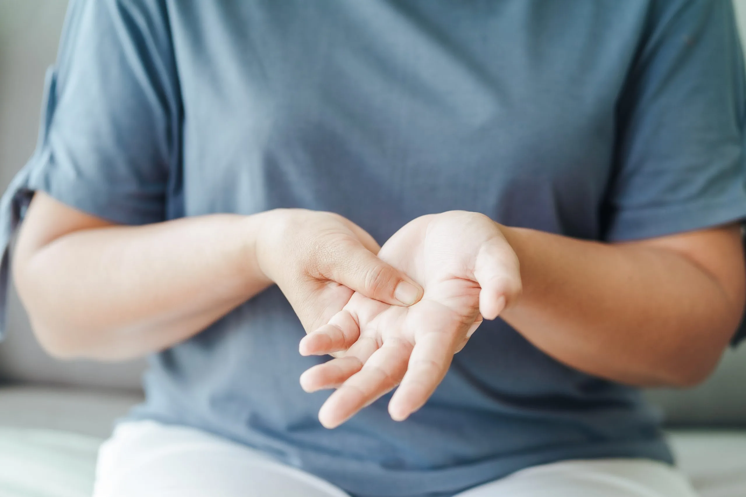 Person in blue shirt examining their open hands for signs of injury or skin condition