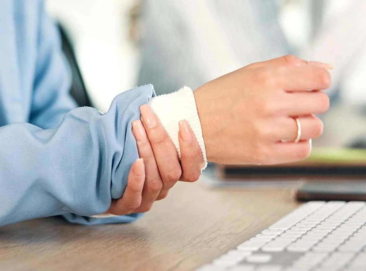 Person wearing blue sleeve with bandaged wrist at desk near keyboard