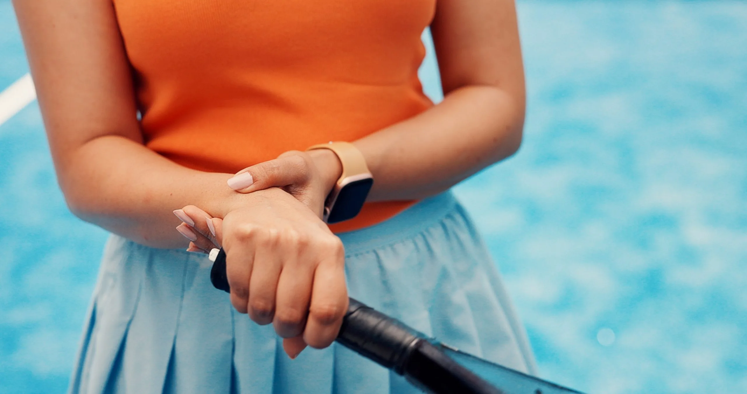 Person in orange top holding a paddle with hands against blue water background