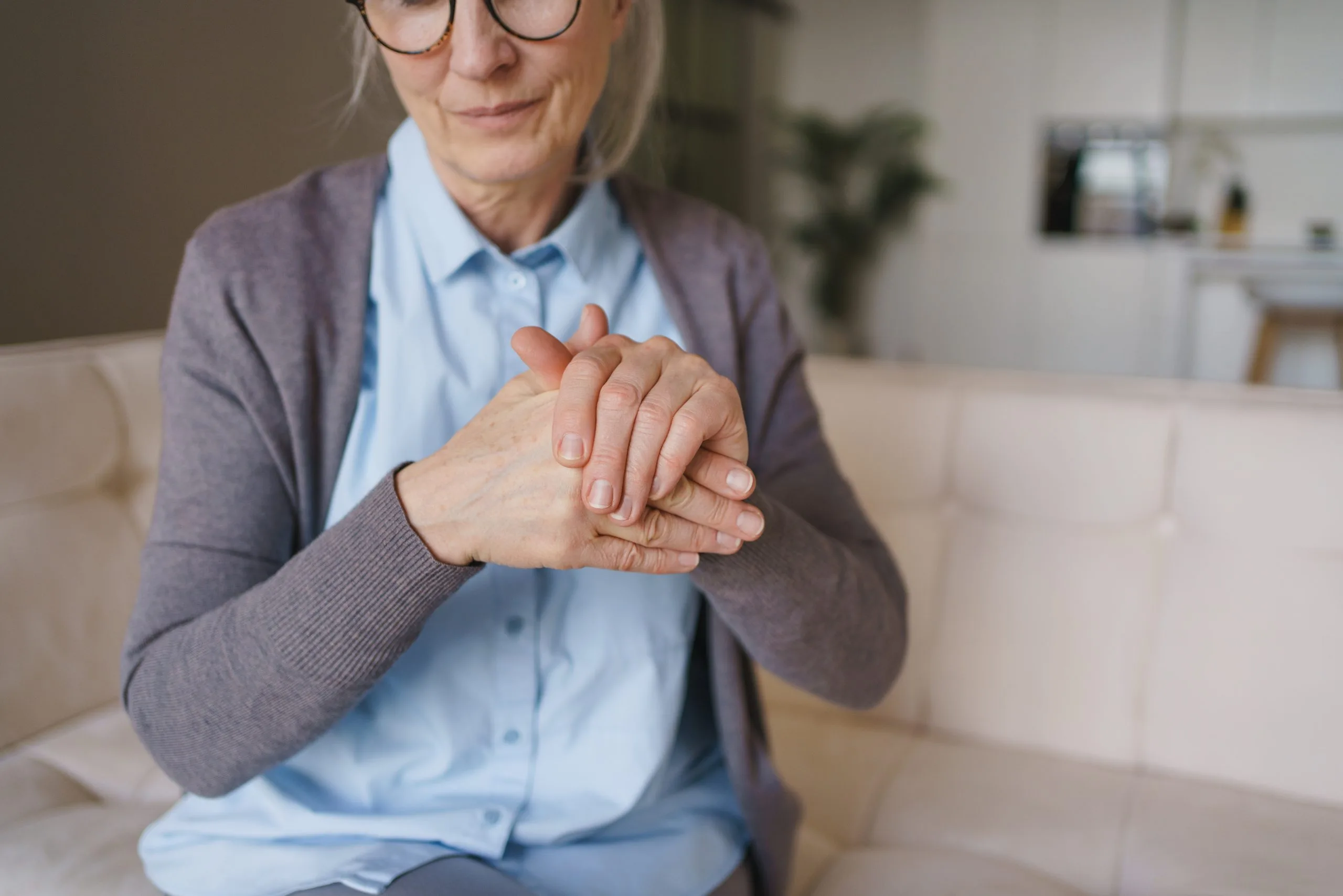 Older woman with glasses resting one hand over the other on her lap