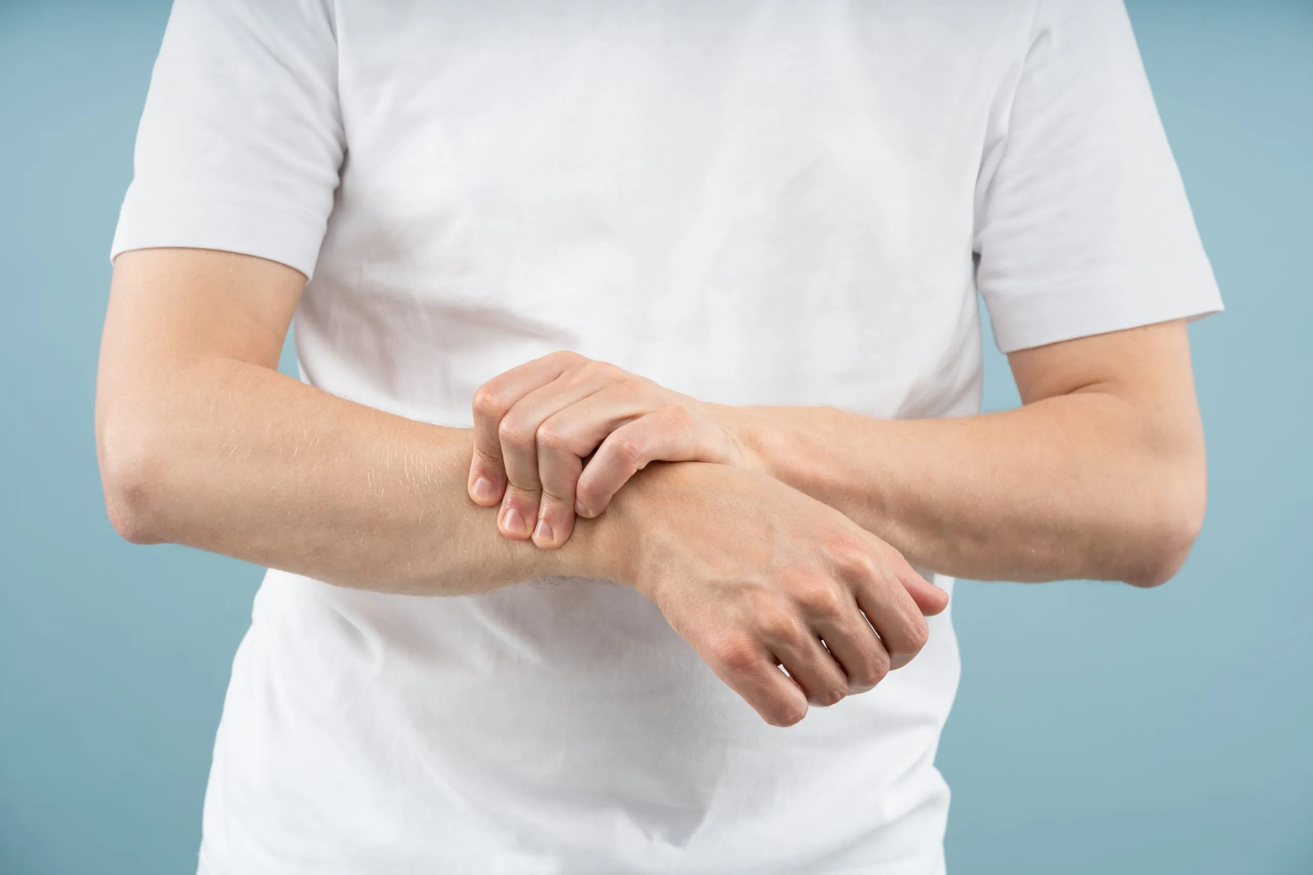 Man in white shirt holding wrist, demonstrating hand or wrist discomfort