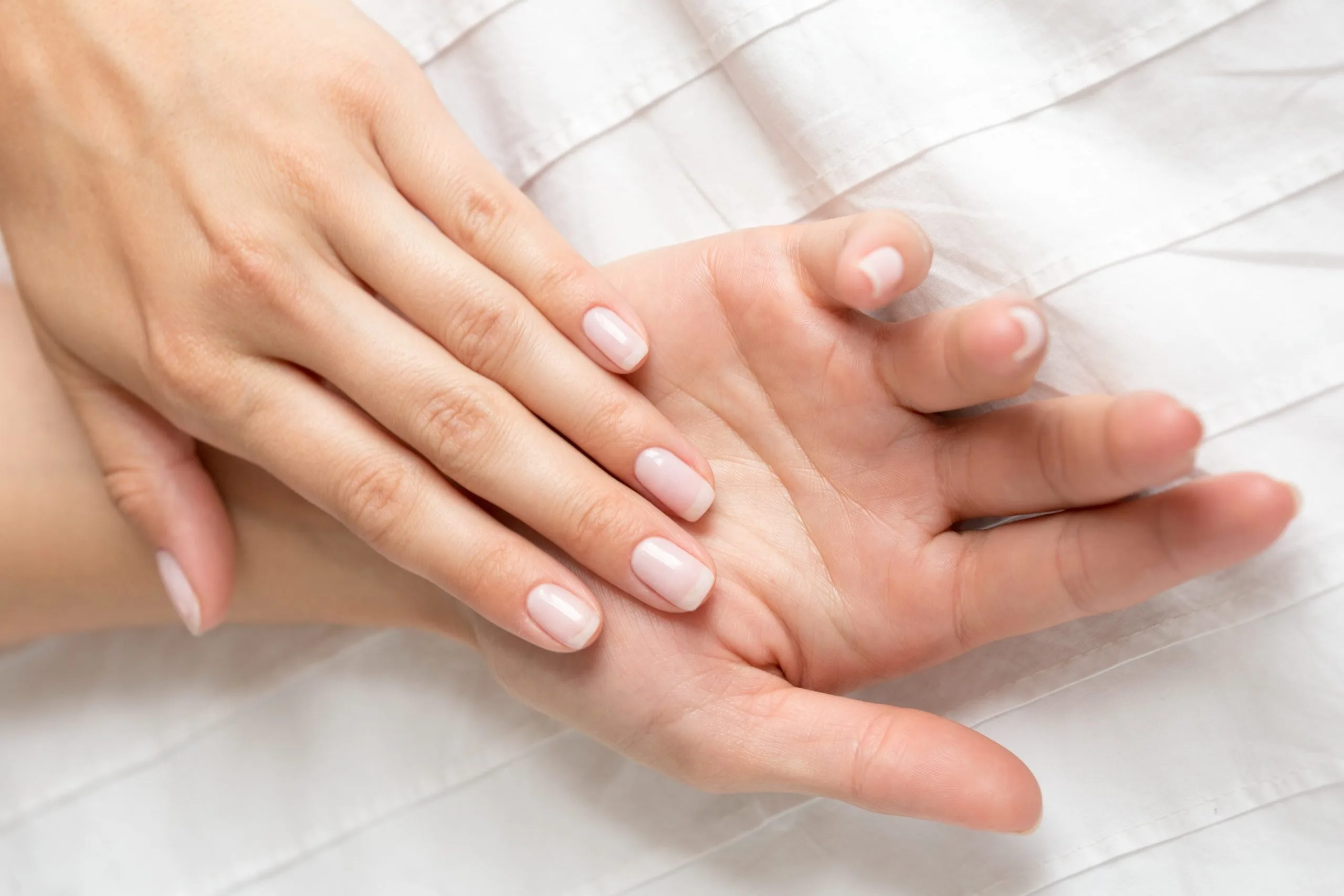 Two hands displaying manicured nails with natural pink and white ombre finish on white fabric