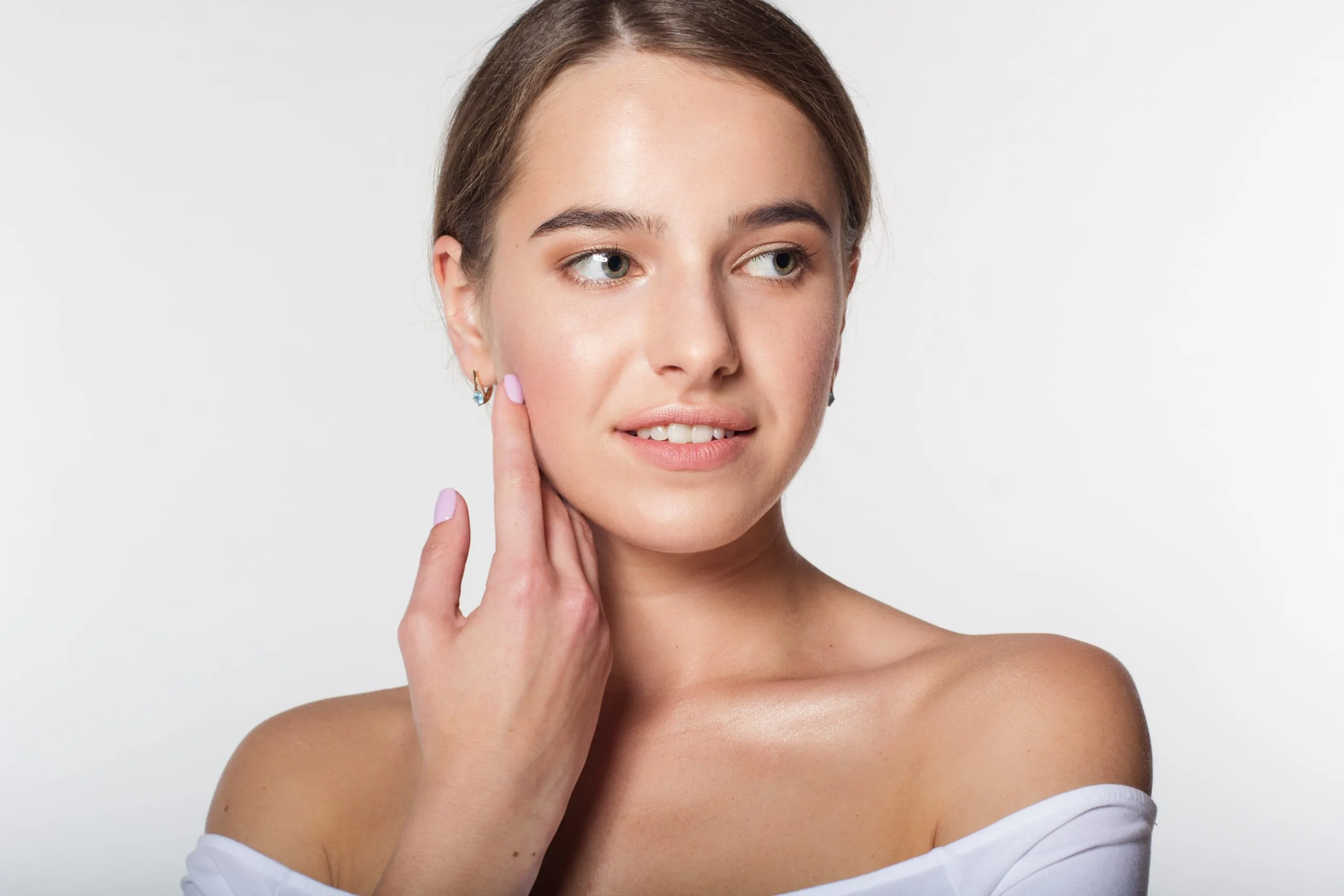 Woman touching her cheek and looking to the side against a neutral background