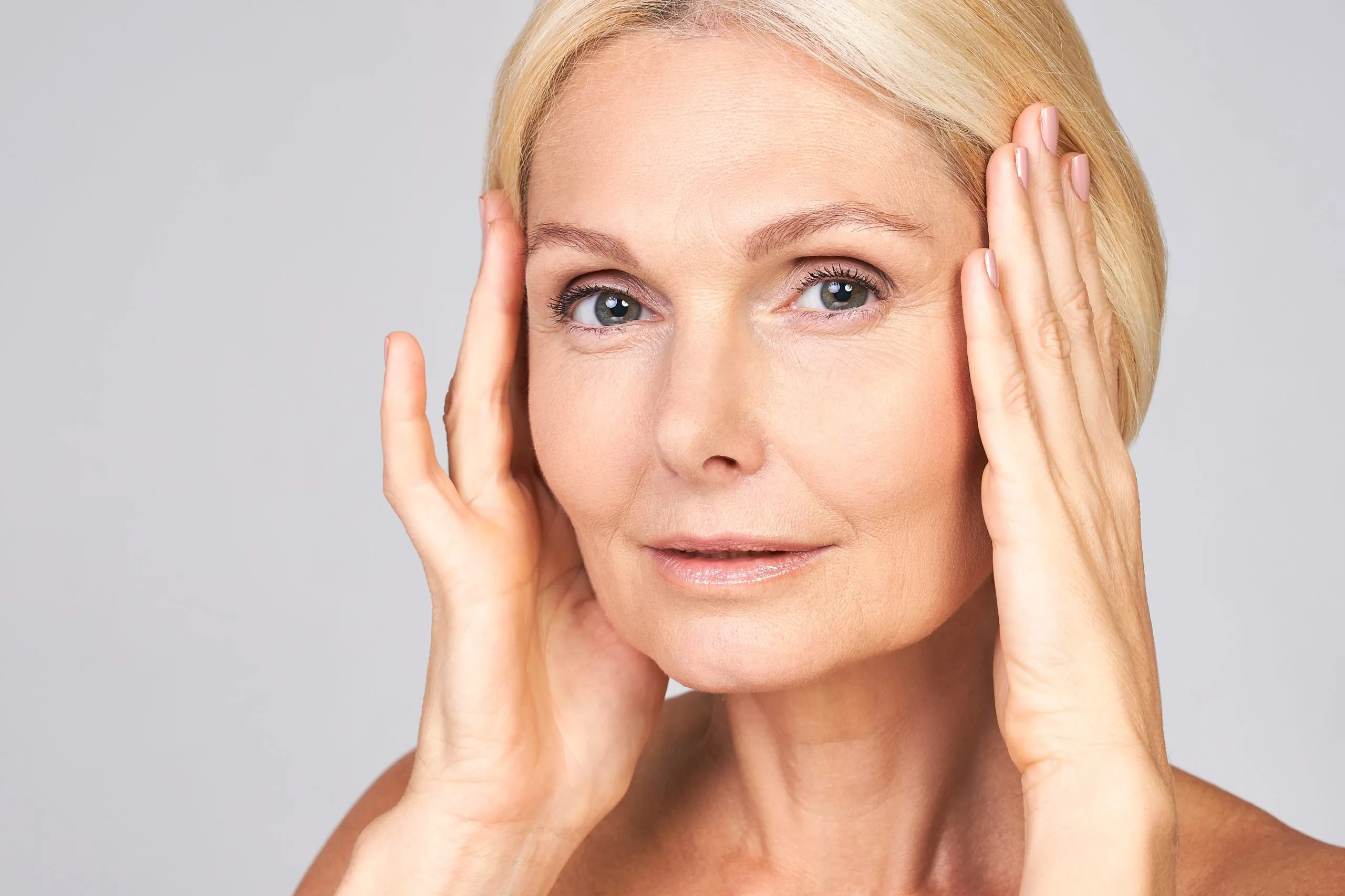 Mature woman with blonde hair touching her face with both hands