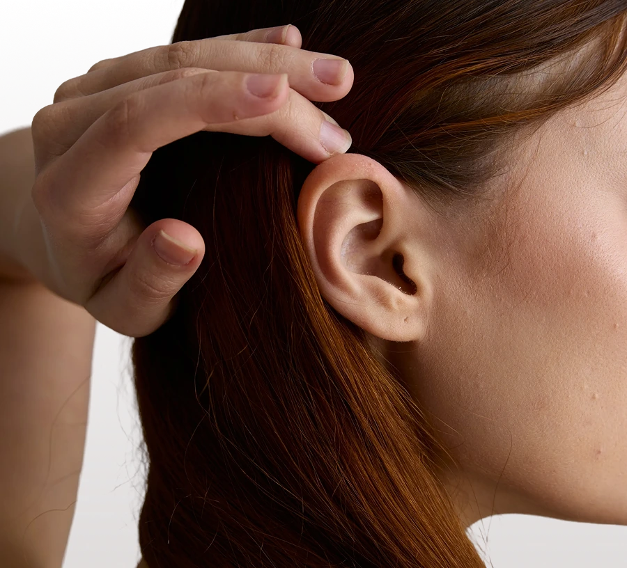 Woman with reddish-brown hair pulling hair back to show earlobe