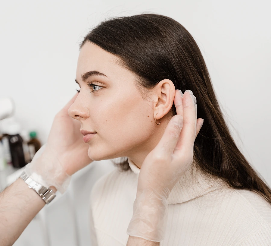 Woman touching her ear with both hands, wearing a light sweater