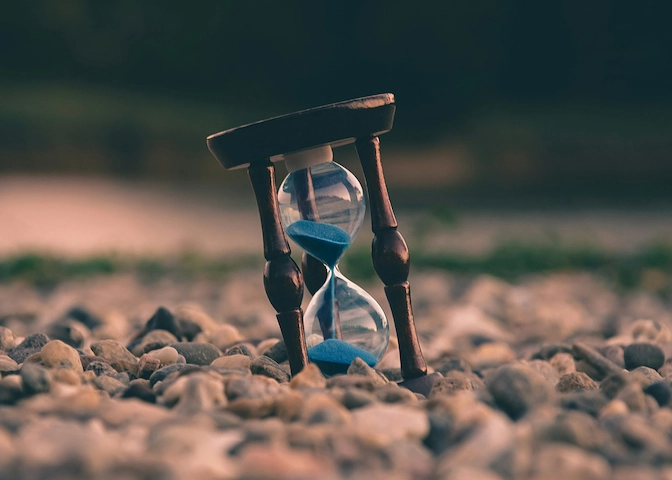 Brown and blue hourglass resting on stones with a softly blurred background