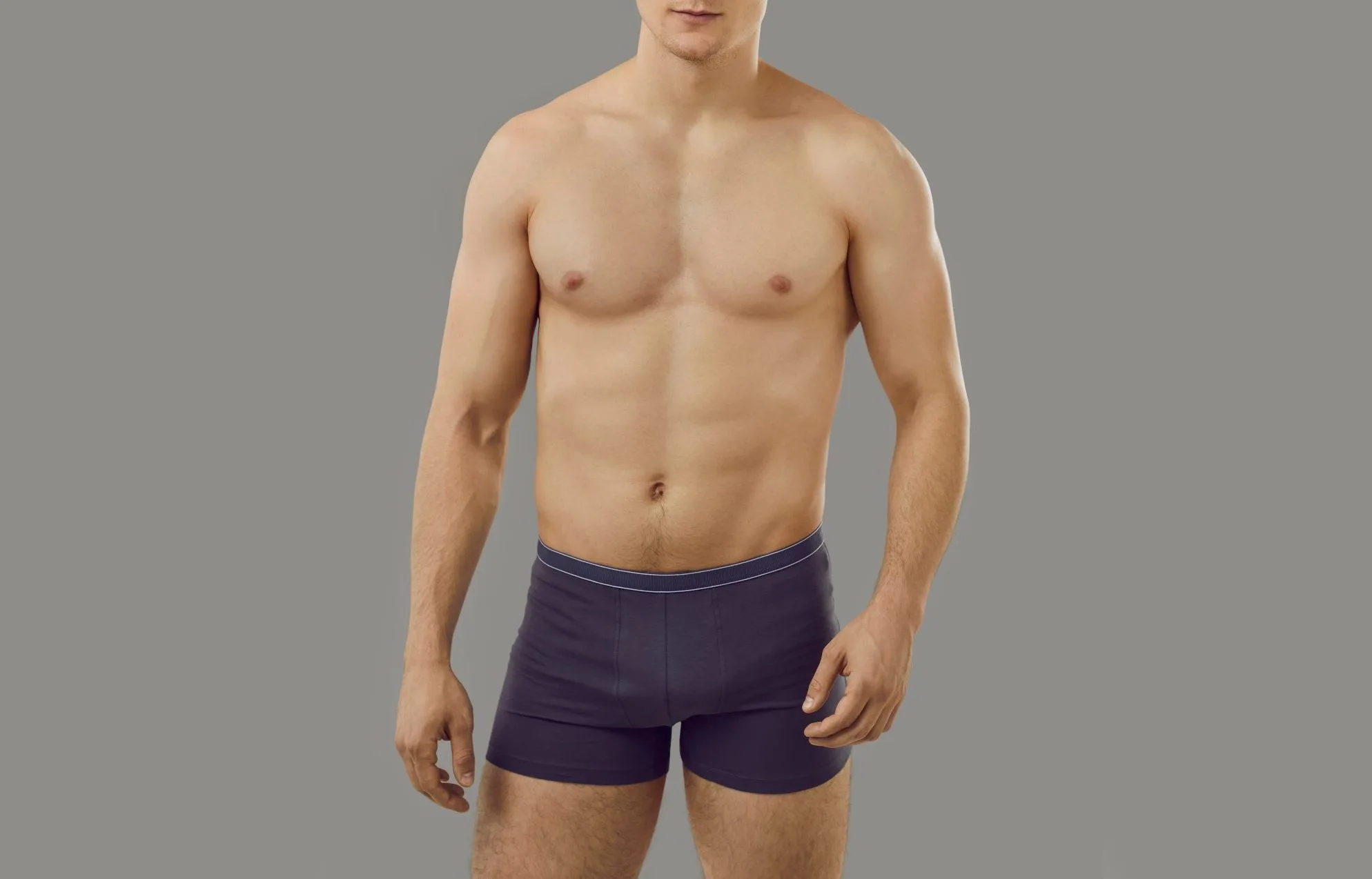 Shirtless man standing against neutral background wearing dark shorts