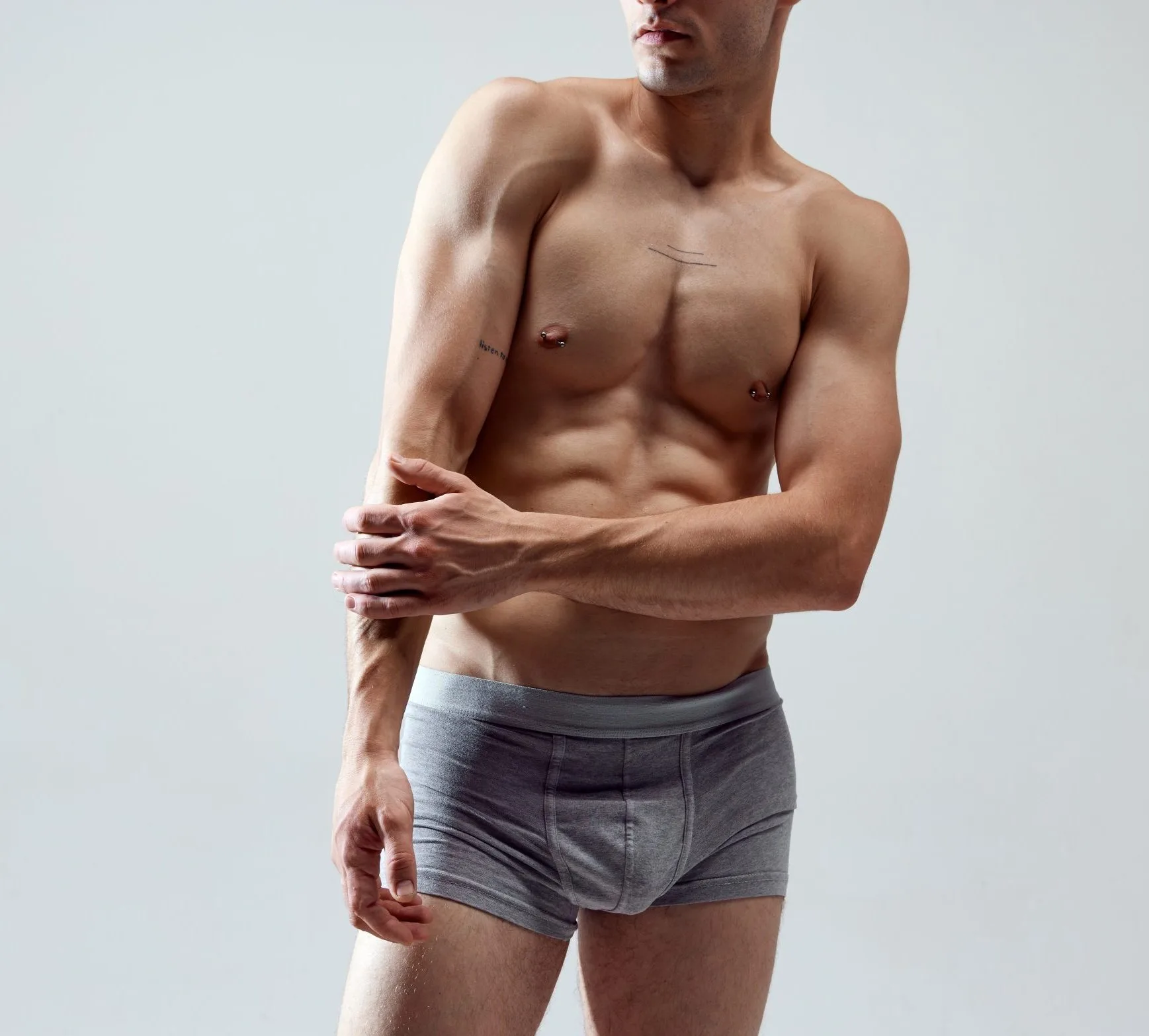 Shirtless man with muscular build posing against neutral background