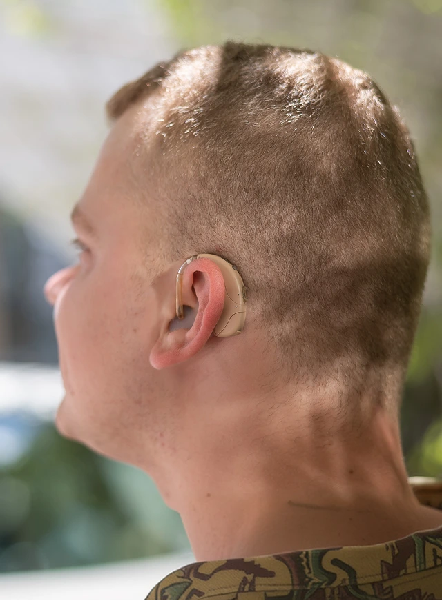 Man wearing a beige behind-the-ear hearing aid, shown in profile outdoors