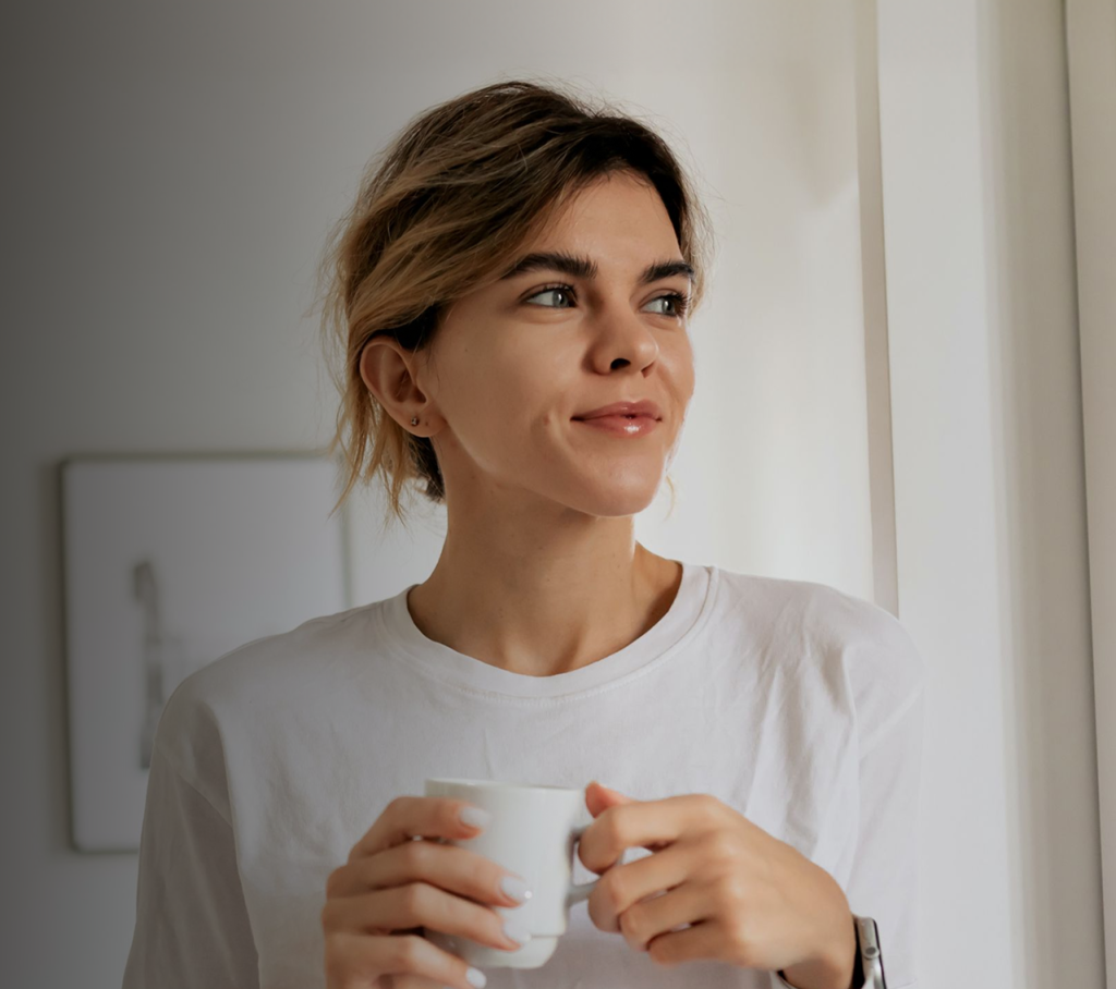 Woman holding a mug in a bright home setting, looking thoughtful