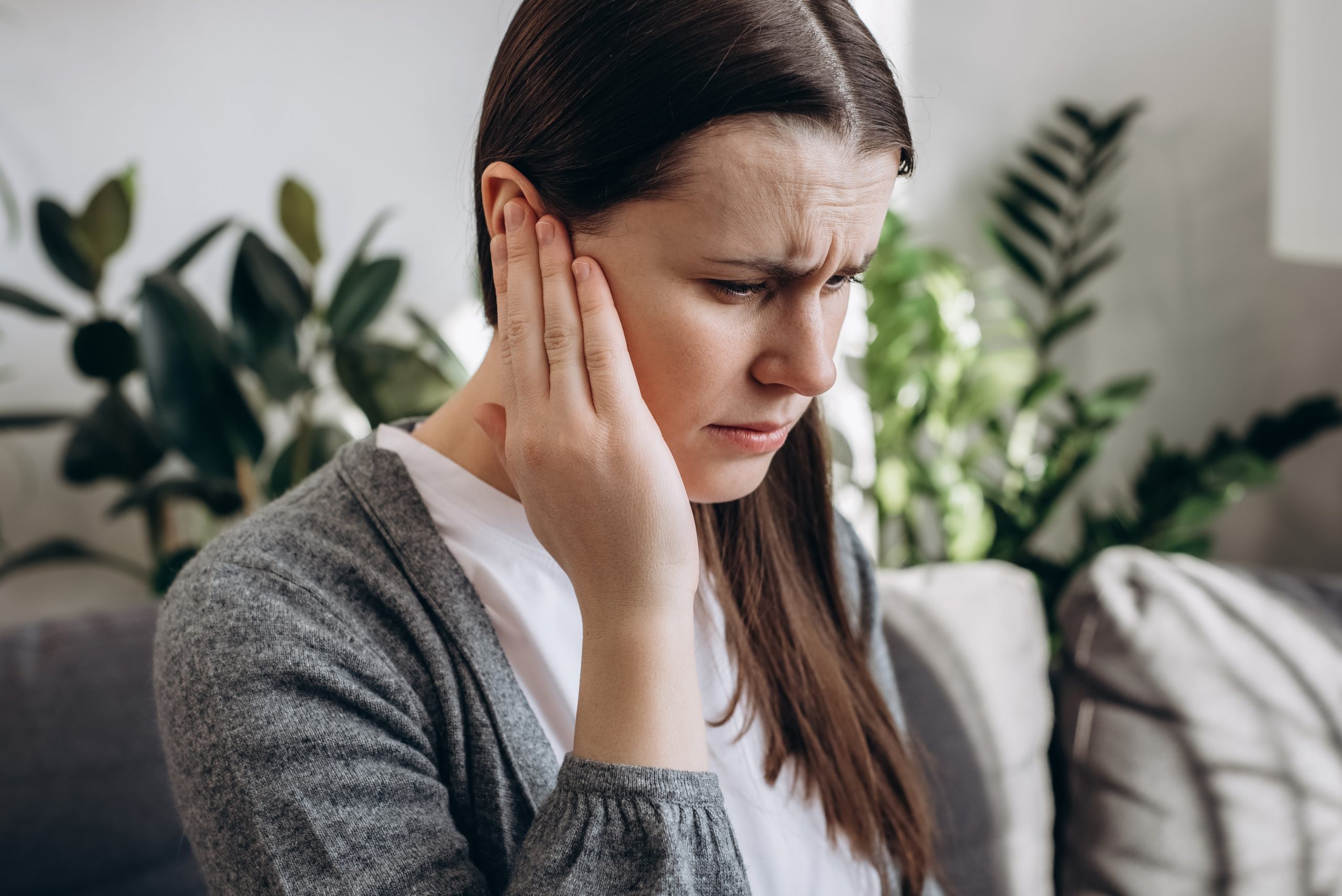 Woman holding her ear with a pained expression, illustrating ear discomfort from sinus or Eustachian tube problems