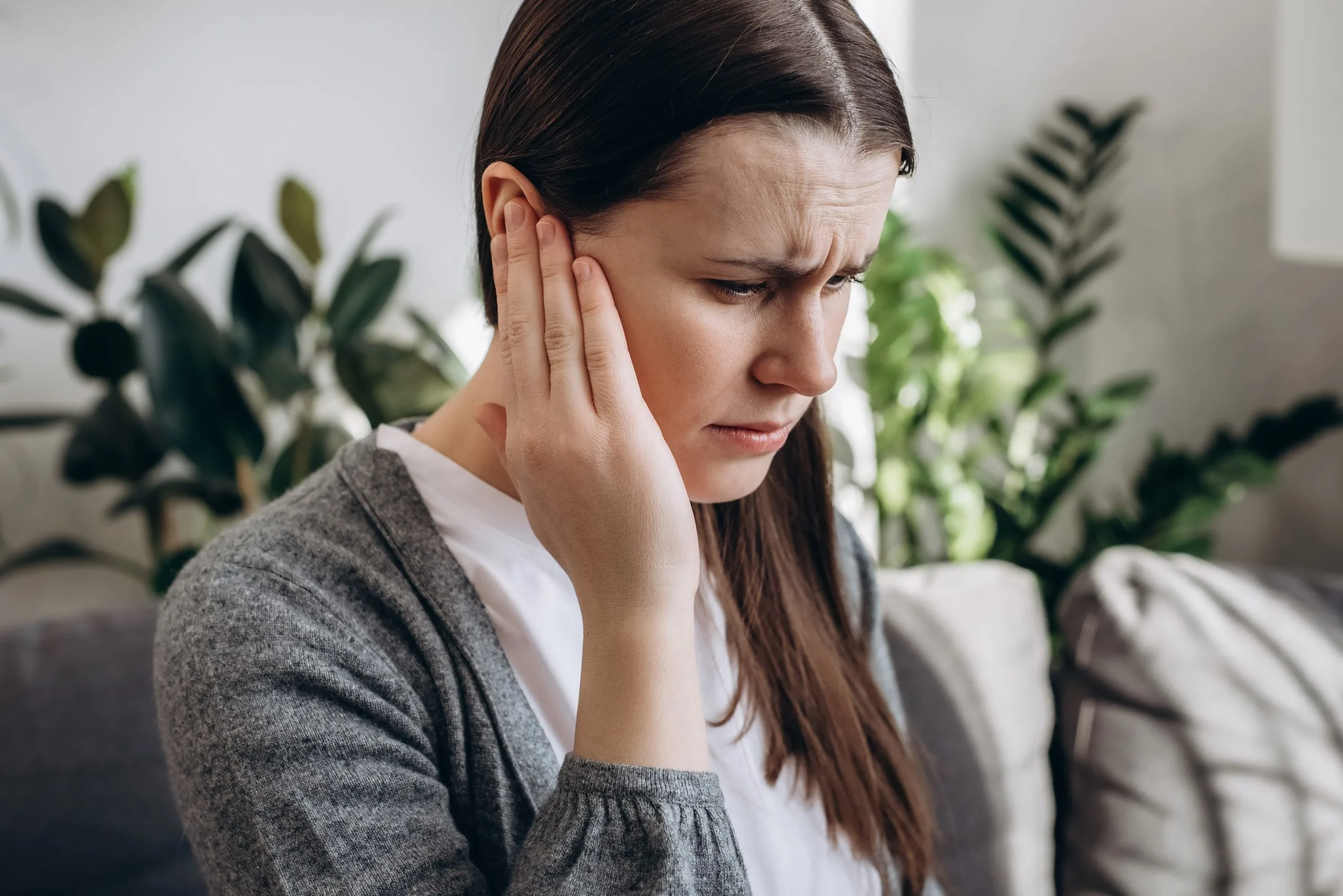 Woman holding her ear with a pained expression, illustrating ear discomfort from sinus or Eustachian tube problems
