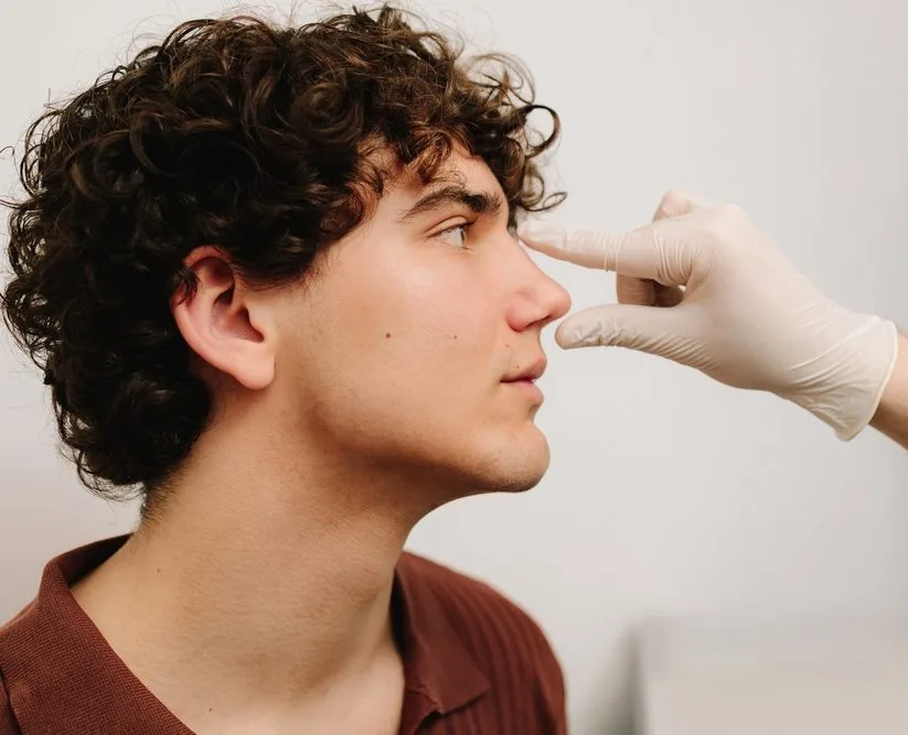 Doctor in white gloves examining a man's nose from the side
