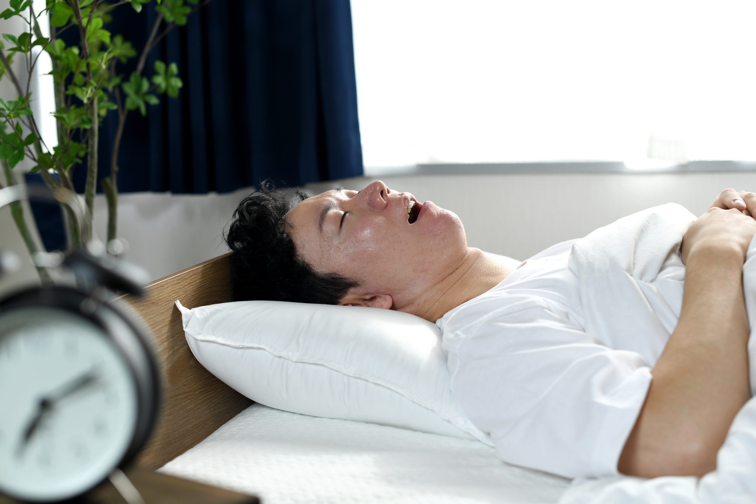 Woman lying in bed with alarm clock on nightstand, appearing to have difficulty sleeping