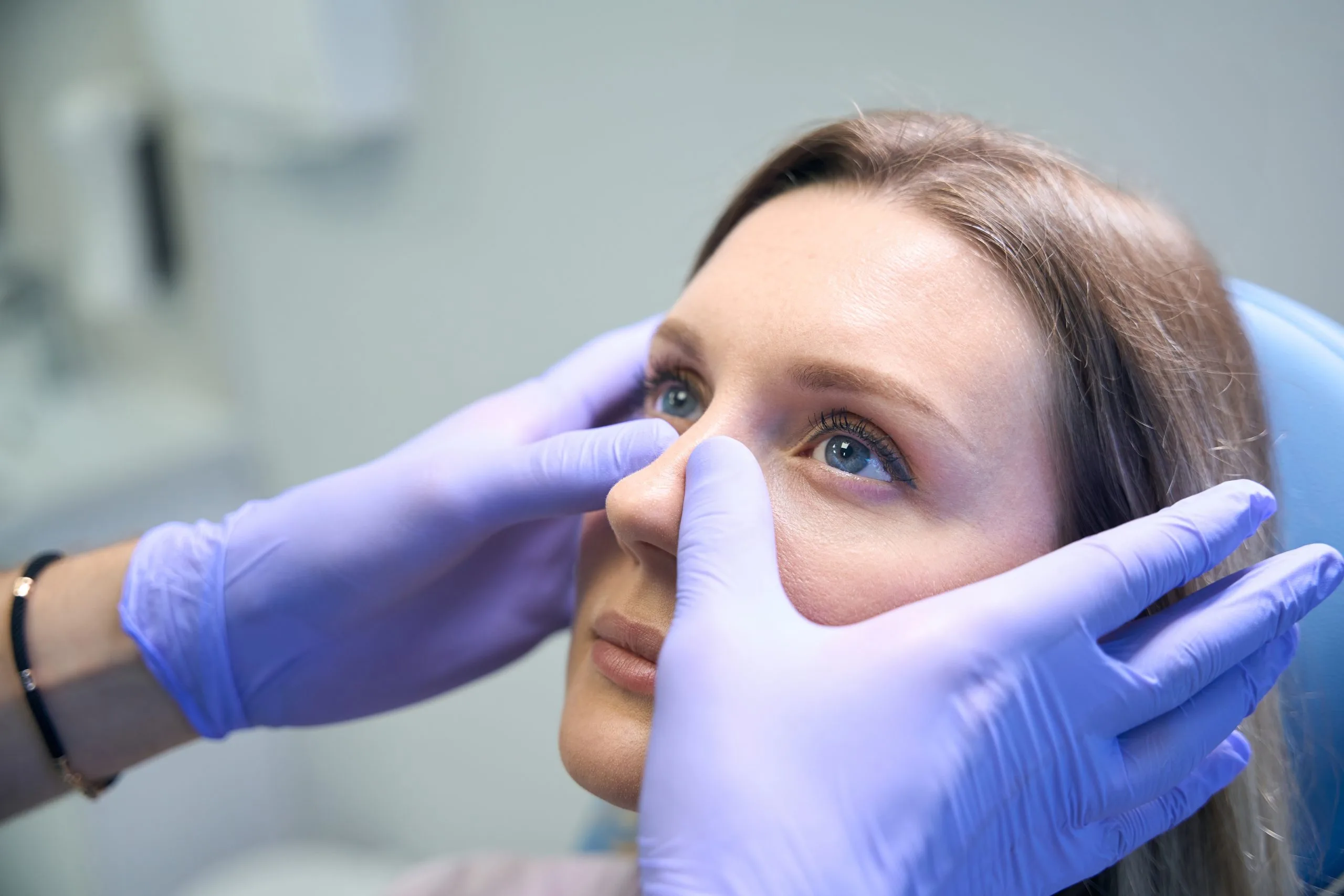Healthcare provider in blue gloves examining patient's nose and sinuses