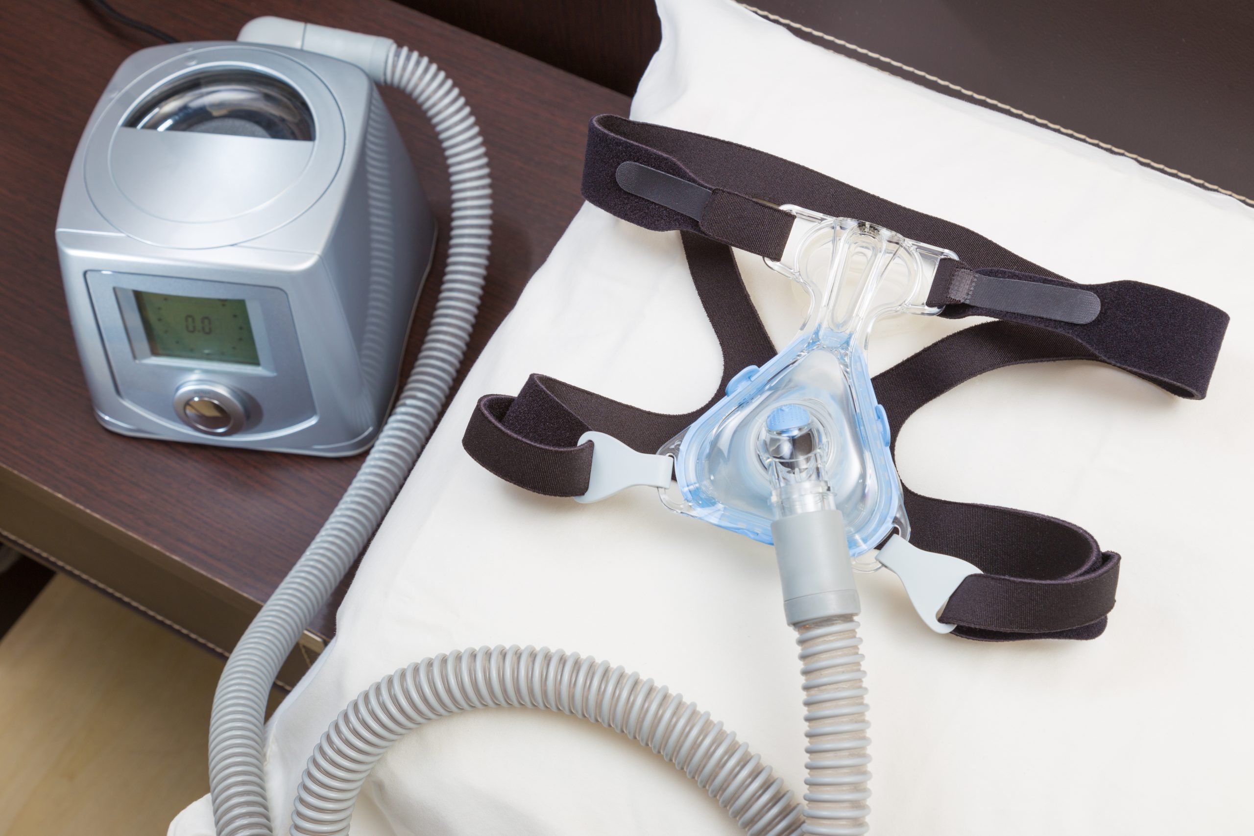 CPAP machine with hose and headgear mask on white pillow