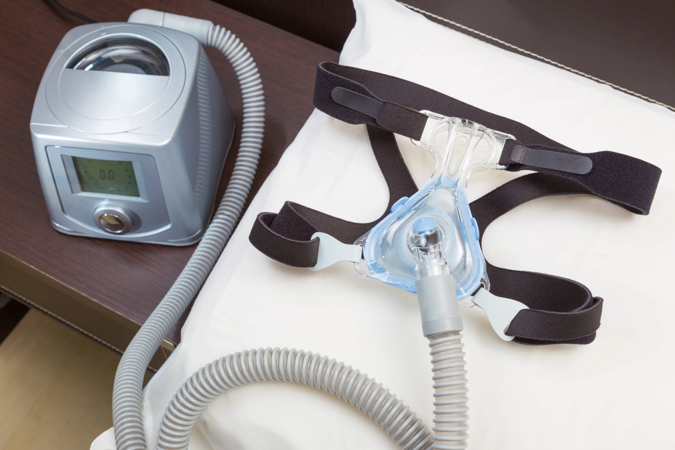 CPAP machine with hose and headgear mask on white pillow
