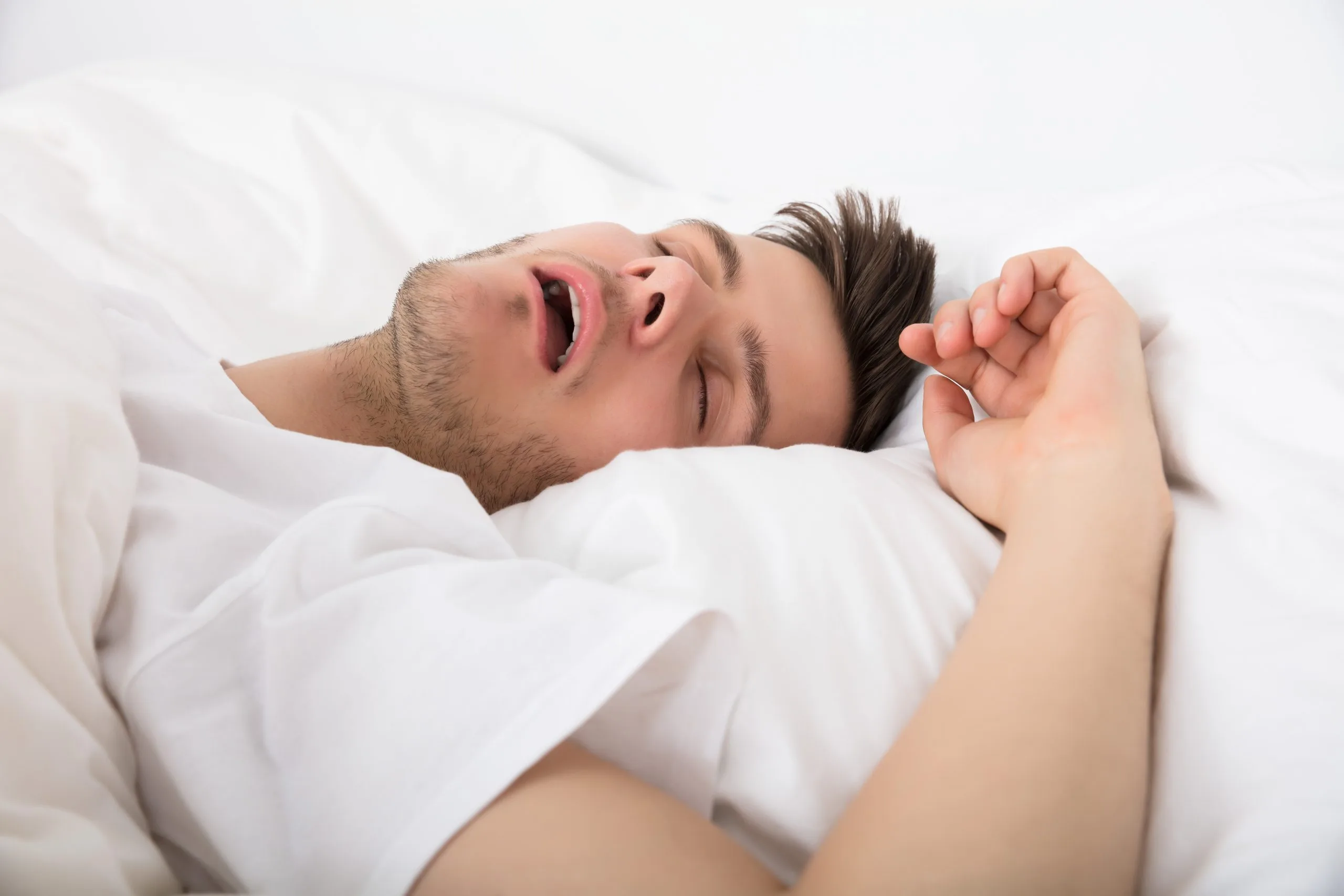 Man snoring while sleeping in bed with white bedding