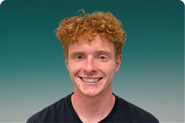 Man with curly red hair smiling at camera against teal background