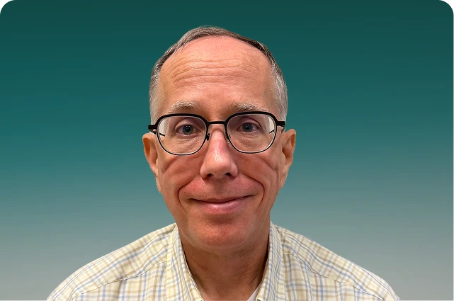 Man with glasses wearing a checkered shirt against a teal background