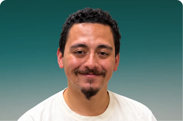 Man with dark hair and mustache smiling at camera against teal background