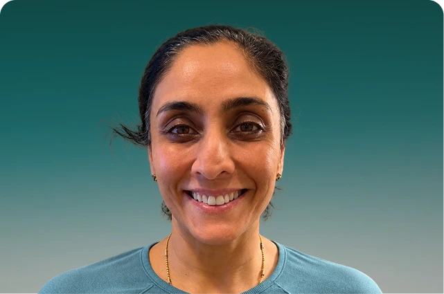 Woman smiling at camera wearing a light blue shirt against a teal background