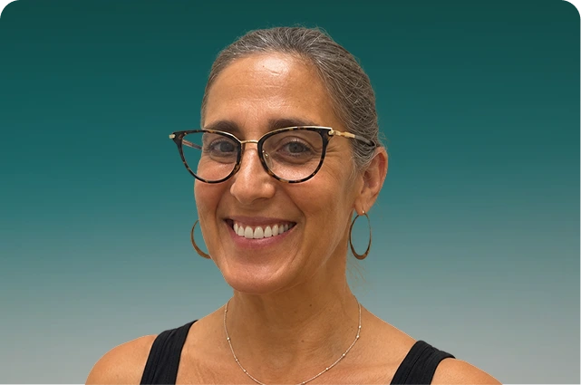 Woman wearing glasses and hoop earrings smiling at camera against teal background