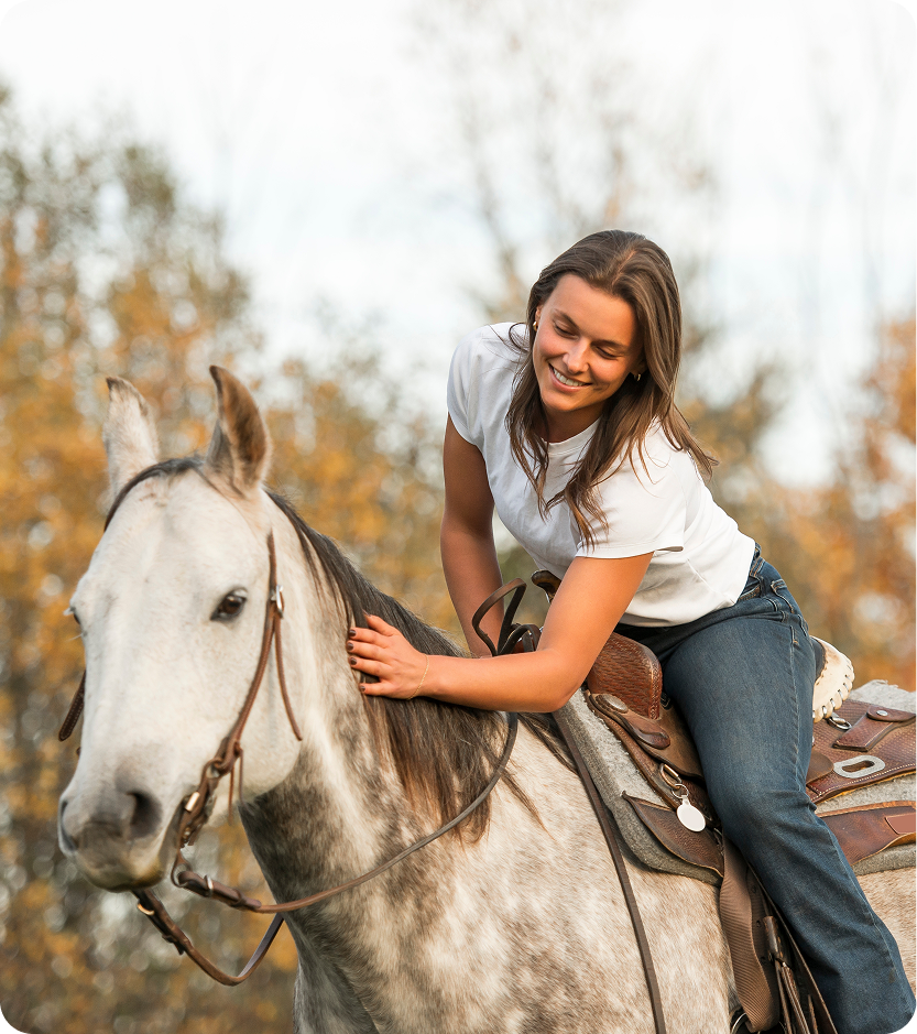 Woman smiling while saddling a gray horse in an autumn field