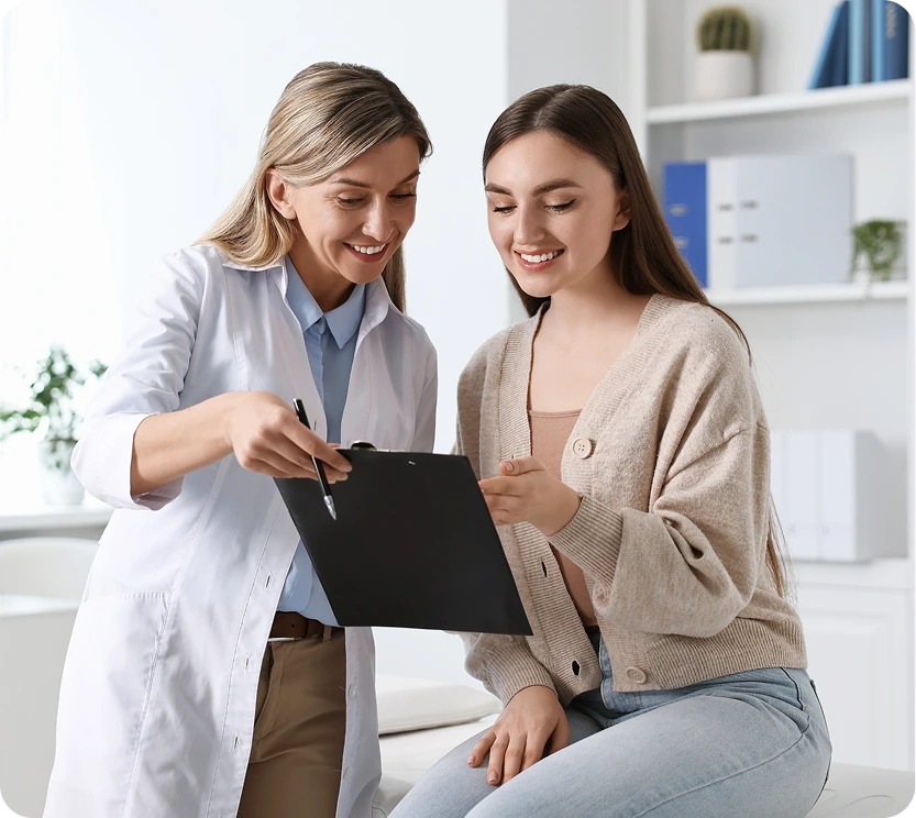 Healthcare provider in white coat reviewing a clipboard with a smiling patient in a bright clinical office